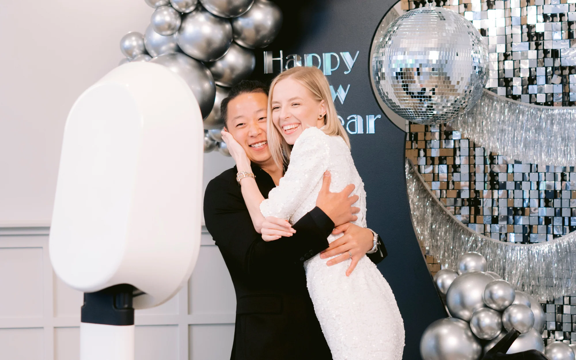 A smiling couple posing beside a Salsa photo kiosk and silver celebration backdrop